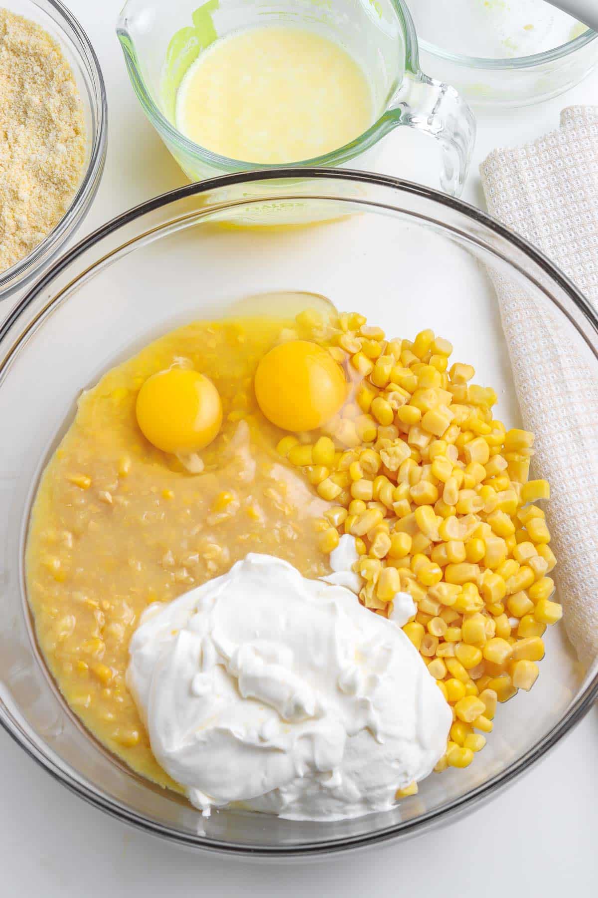 Glass mixing bowl of eggs, corn, creamed corn and sour cream.