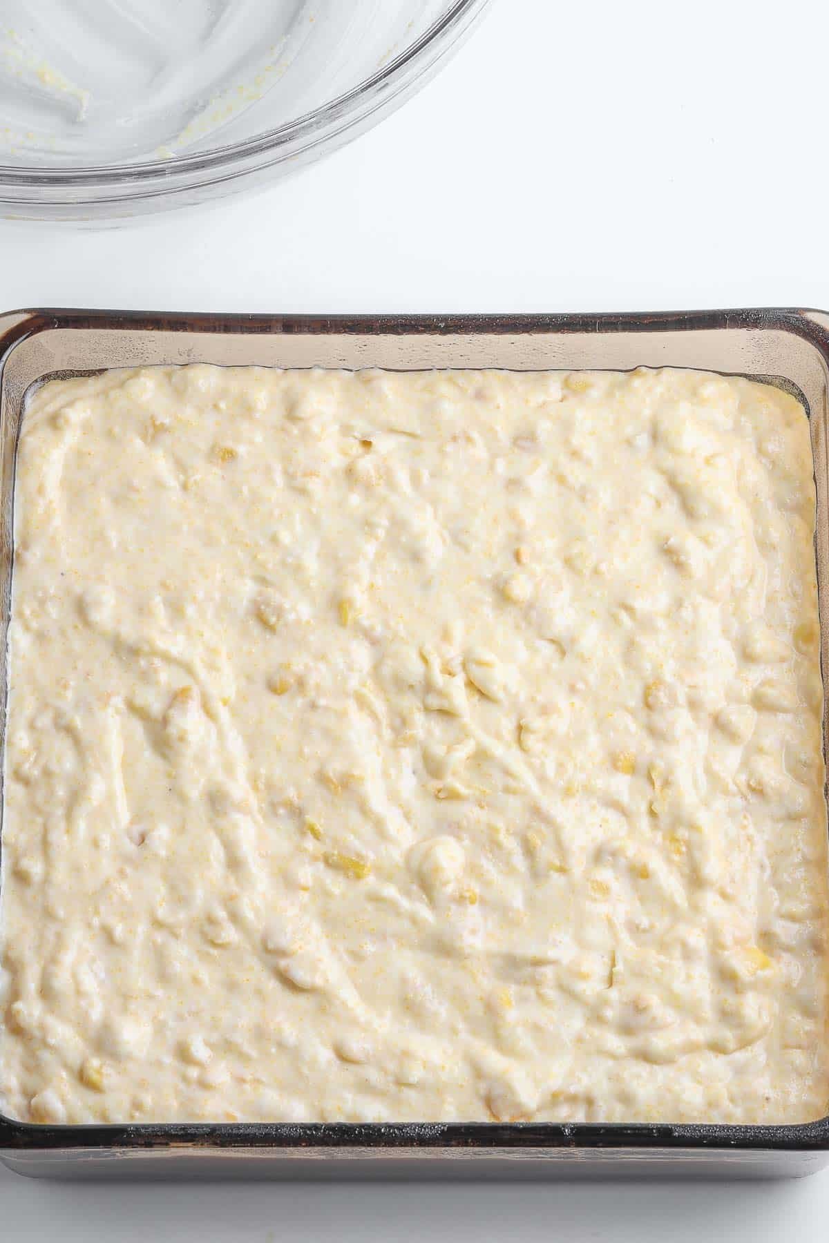 A baking dish with a corn casserole mix in it.