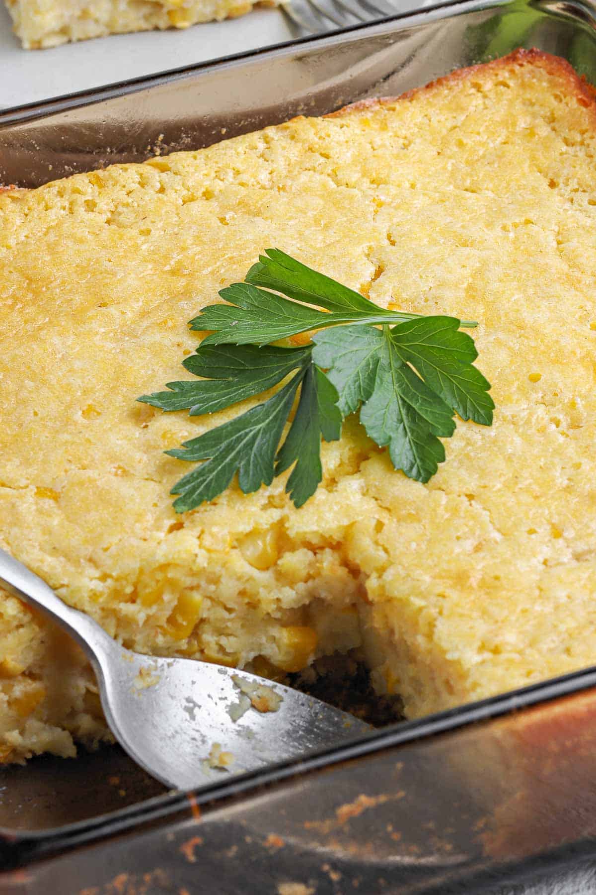 Corn casserole in a baking dish with a slice removed.
