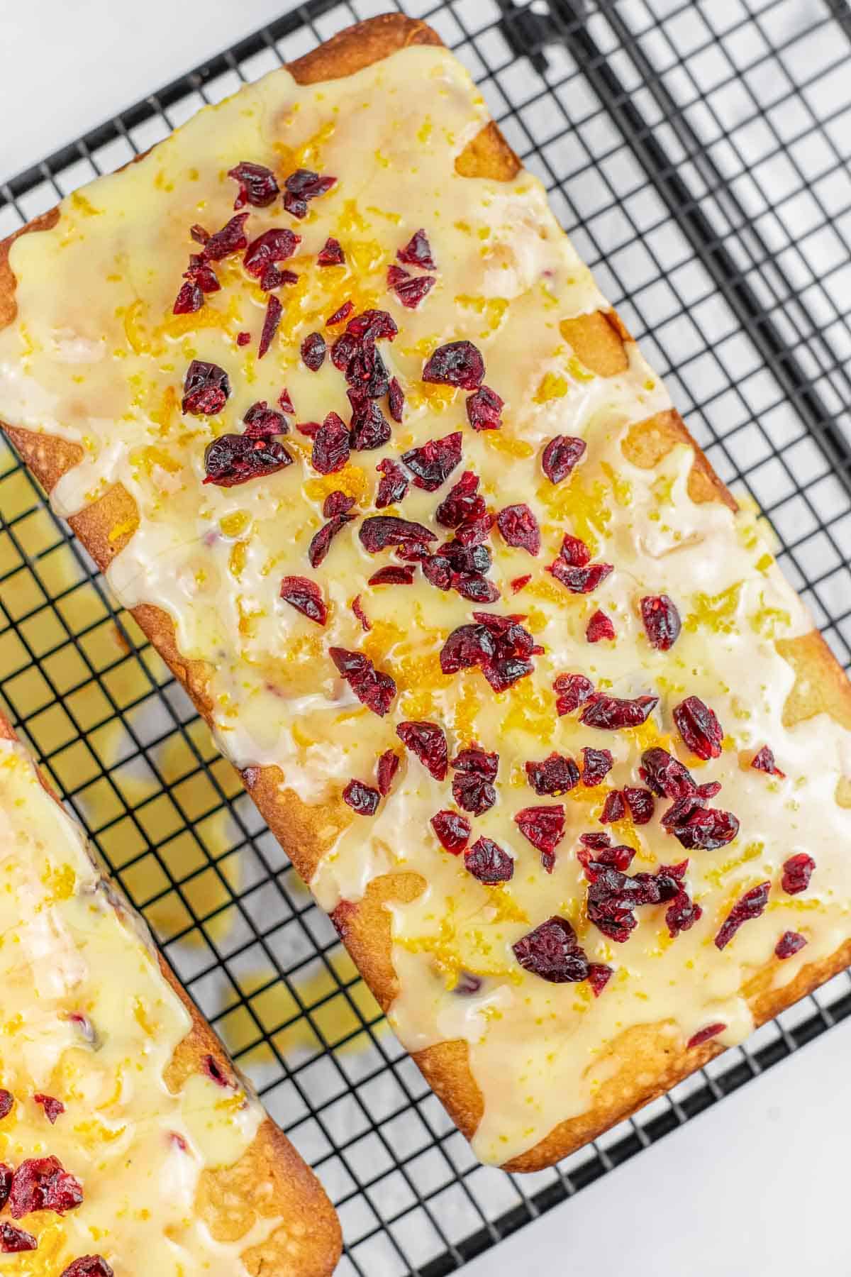 loaf of orange cranberry bread topped with orange glaze and chopped dried cranberries on a cooling rack.