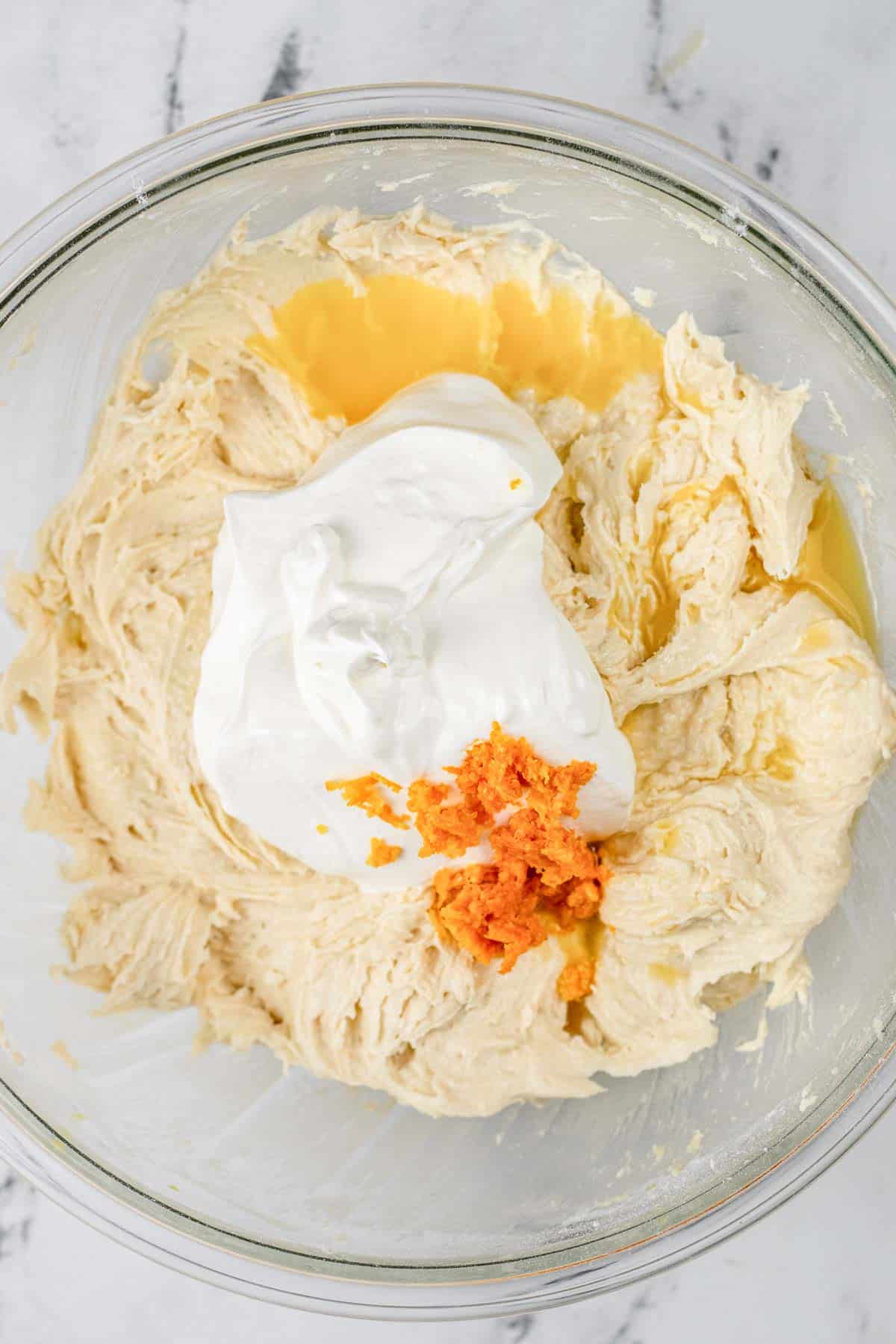 Bread batter topped with sour cream and orange zest in a glass bowl.