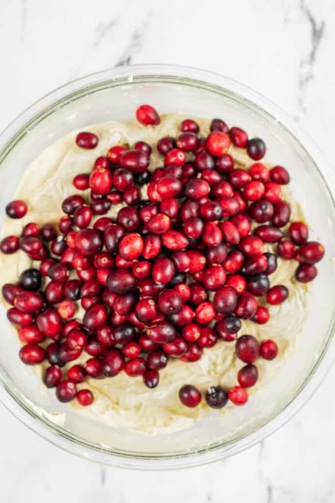 fresh cranberries over bread batter in a glass bowl.