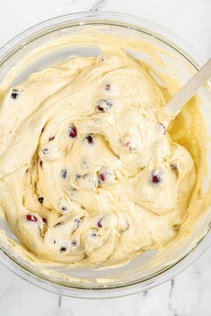 A glass bowl of batter with cranberries in it.