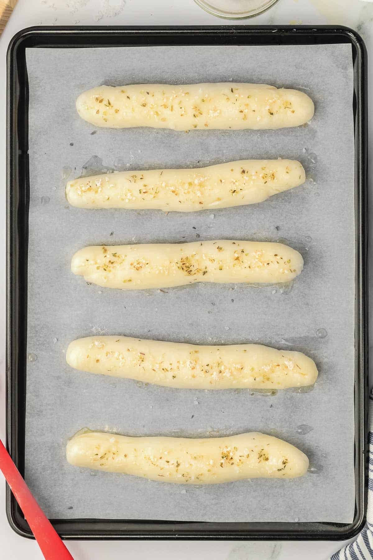 A baking sheet with garlic breadsticks on it.