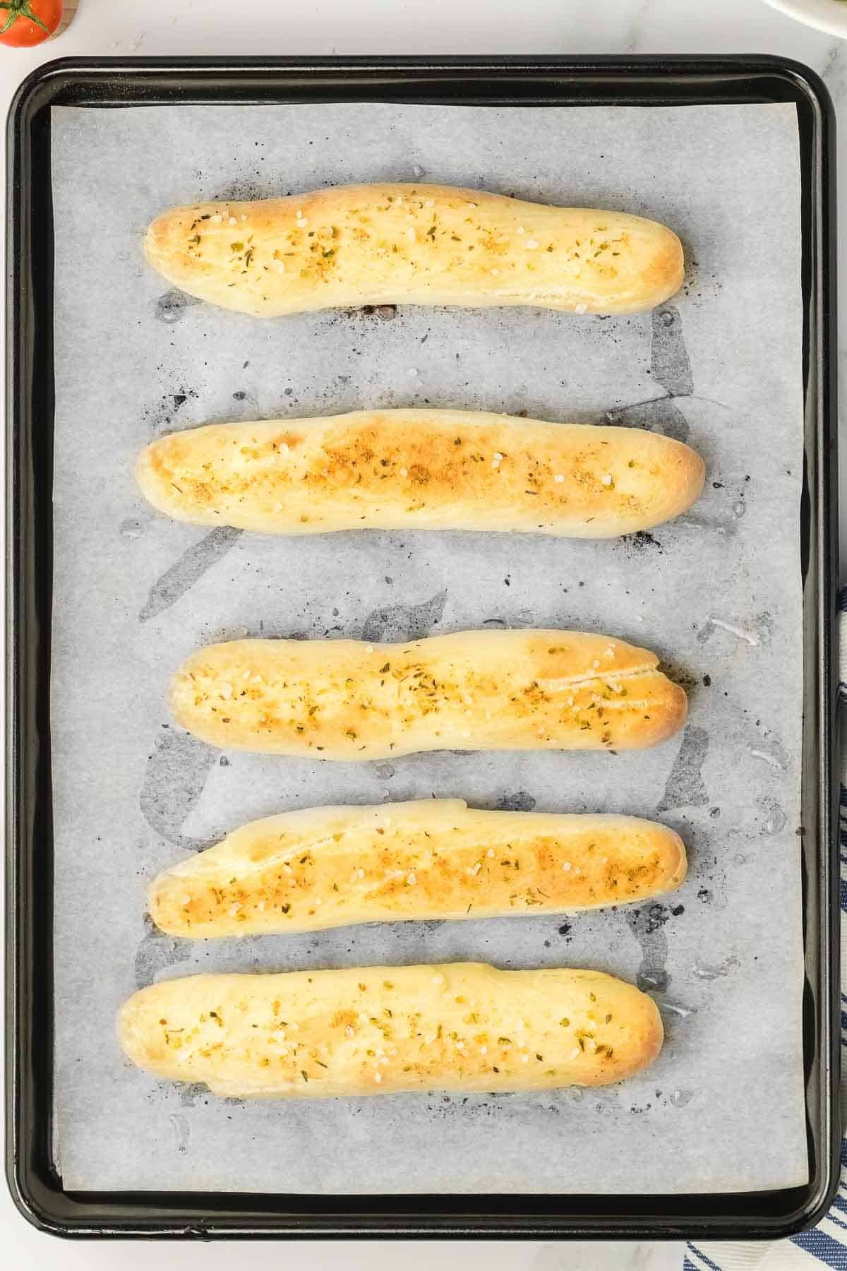 Buttery garlic breadsticks on a baking sheet.