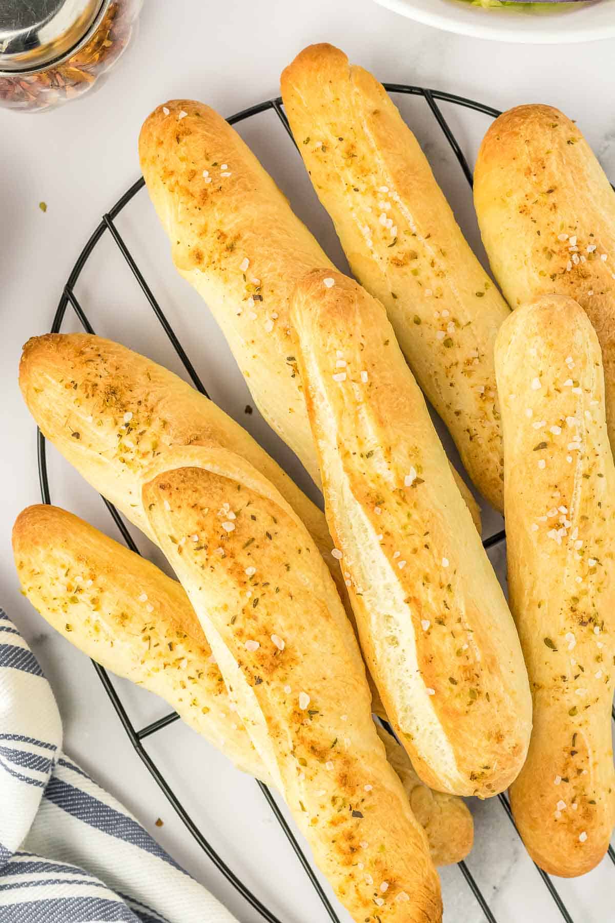 A wire rack with several garlic breadsticks stacked together.