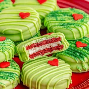 A red plate of Grinch oreos with green frosting and candy hearts on it.