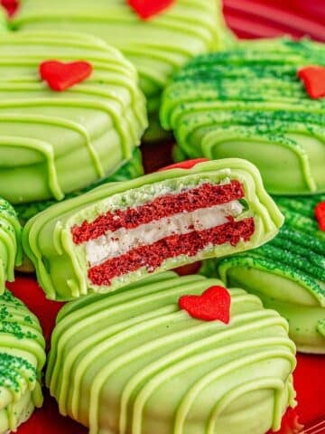 A red plate of Grinch oreos with green frosting and candy hearts on it.