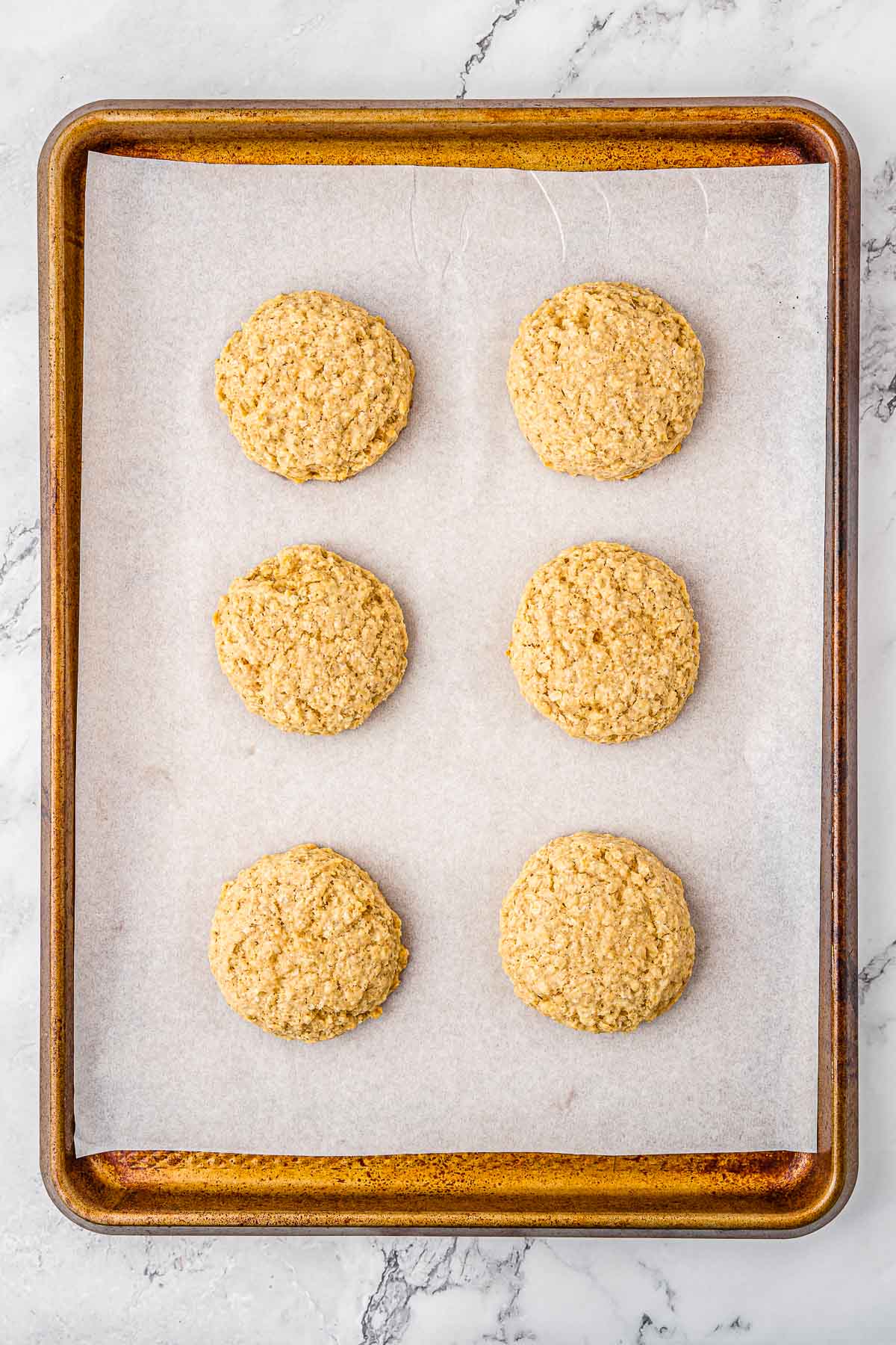 Six oatmeal cookies on a baking sheet.