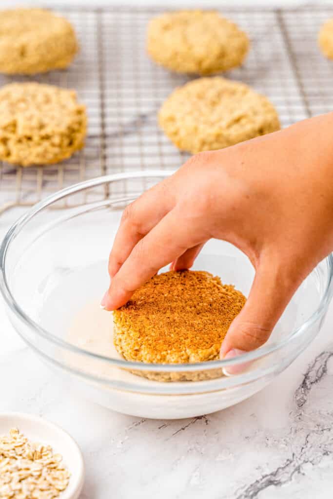 A person dipping an oatmeal cookie in a bowl of icing.