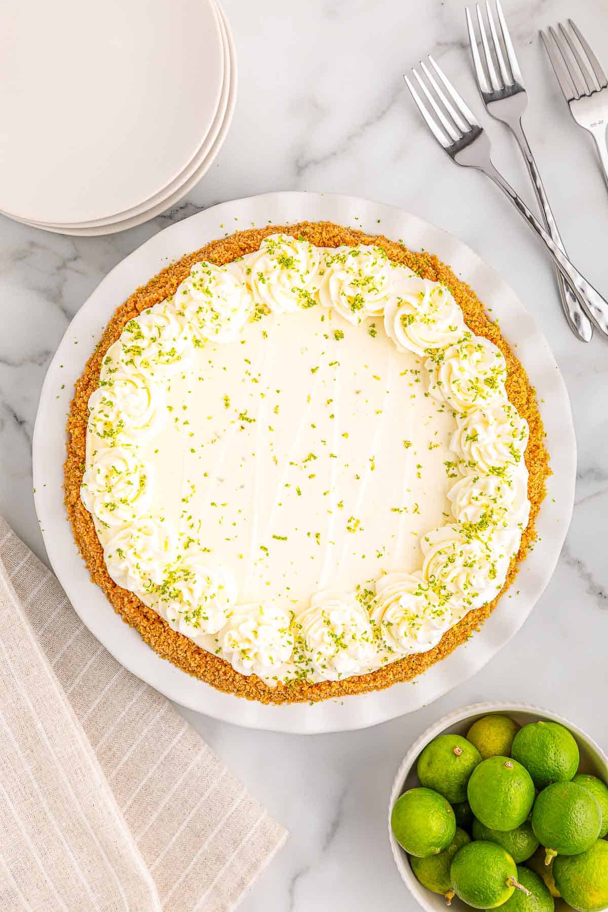 A key lime pie piped with whipped cream and garnished with lime zest on a white plate.