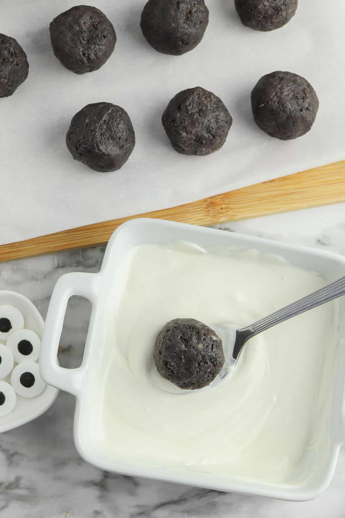 A bowl of melted white chocolate with a spoon holding an oreo ball over top.