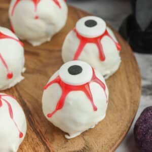 several white and red oreo cookie eyeball truffles on a wooden cutting board.