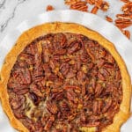 best pecan pie recipe in a white pie plate surrounded by pecan halves.