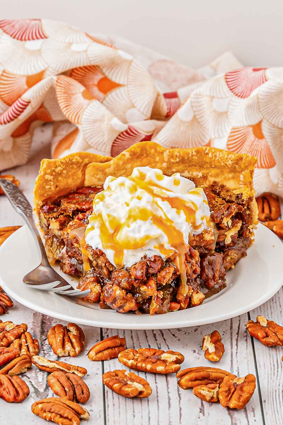 A slice of pecan pie topped with whipped cream and caramel drizzle with fork.