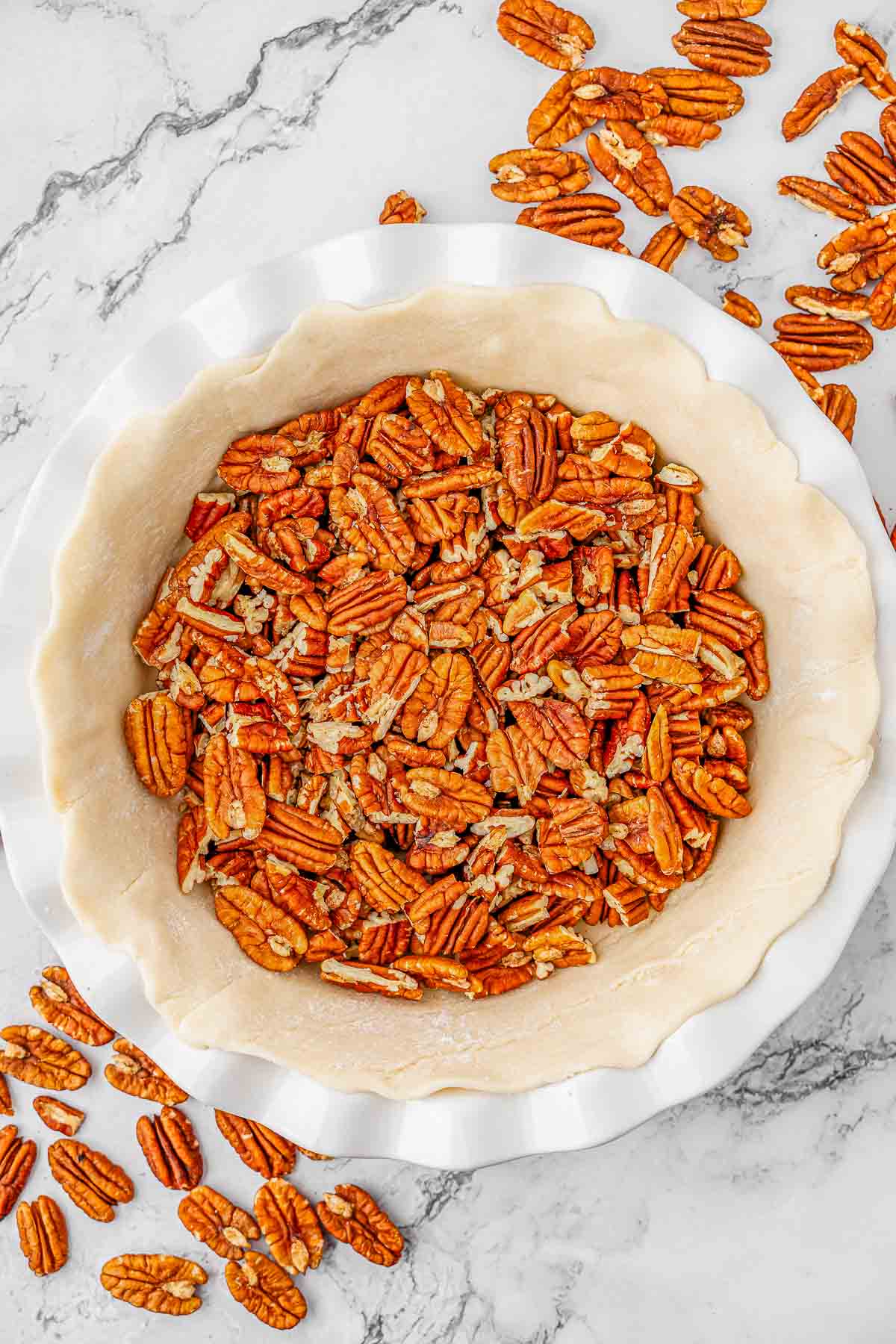 A pie crust filled with pecans on a white plate.