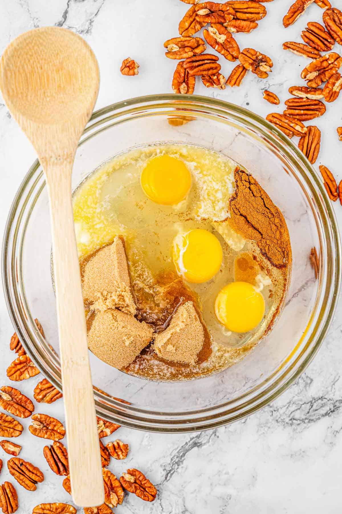 Eggs, corn syrup, light brown sugar, melted butter, vanilla extract, ground cinnamon, and salt being mixed in a glass bowl.