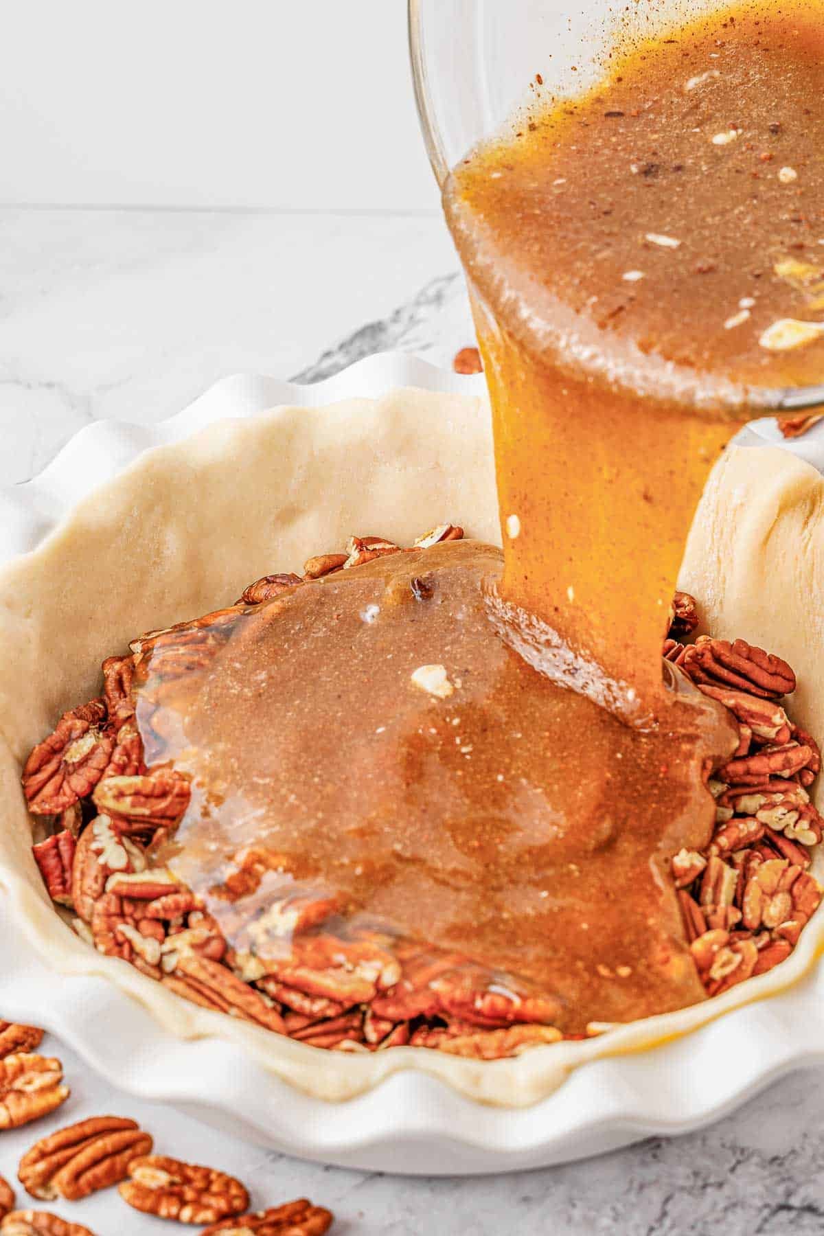 Sauce mixture being poured over pecans in a pie crust.