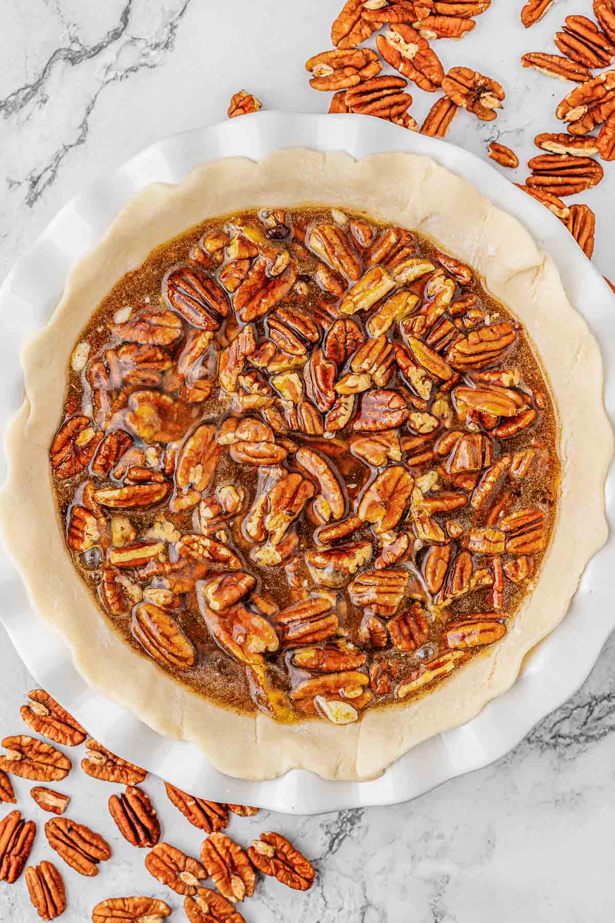 Unbaked pecan pie on a white plate with pecans around it.
