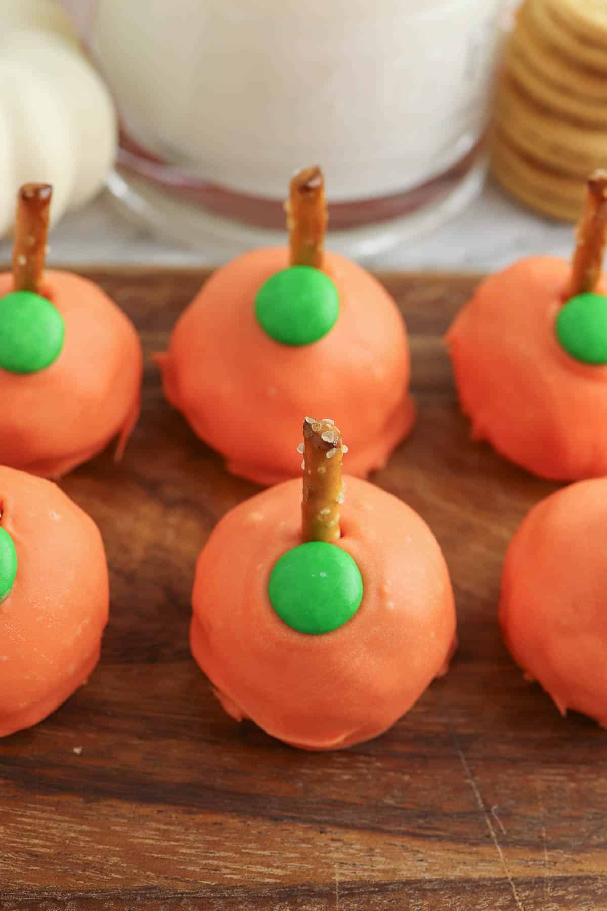 pumkin oreo truffles with pretzel stem and M&M leaf on a cutting board.