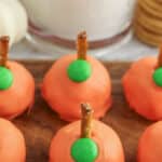 A group of orange pumpkins with green pretzels on a wooden cutting board.