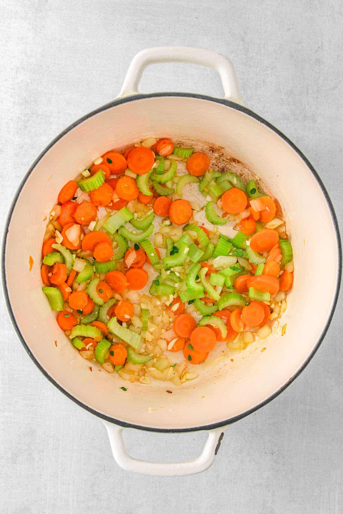 A white cooking pot filled with carrots, celery and onions.