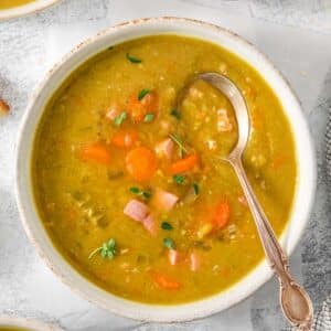 A bowl of classic split pea soup with ham with a spoon in it.