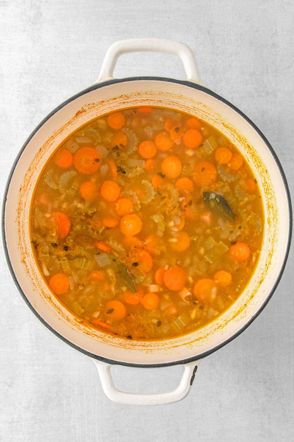 A white pot of soup with celery and carrots in it.