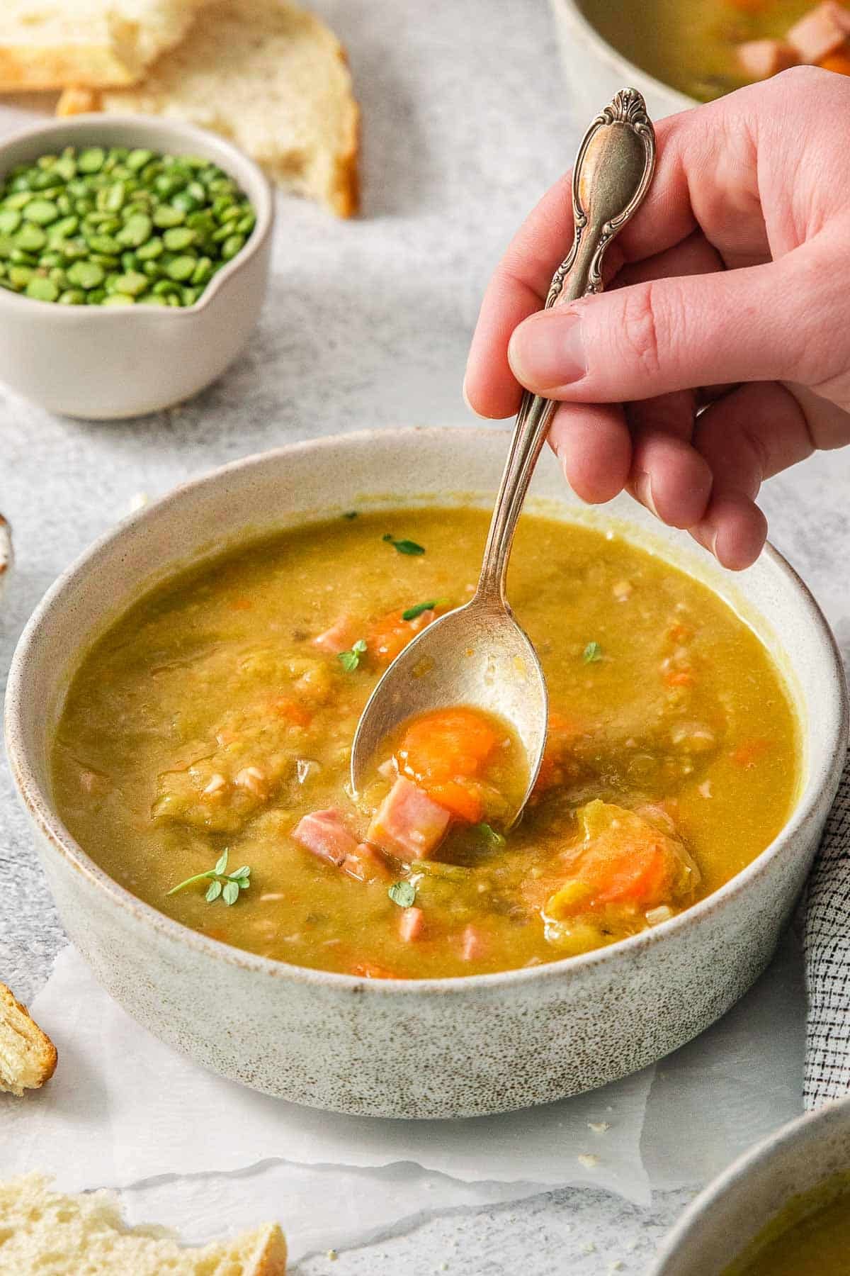 A hand holding a spoonful of split pea soup over a white bowl.