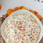 A bowl of funfetti dip topped with orange and chocolate sprinkles and surrounded by chocolate animal crackers and vanilla wafers.