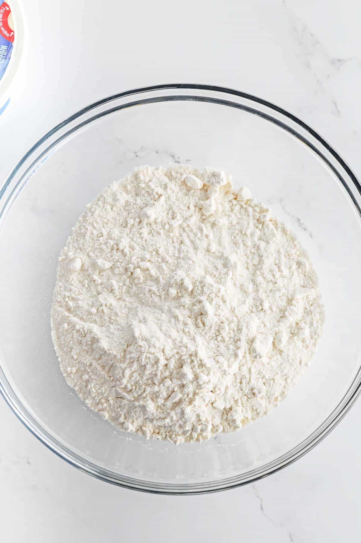 A glass mixing bowl of dry white cake mix.