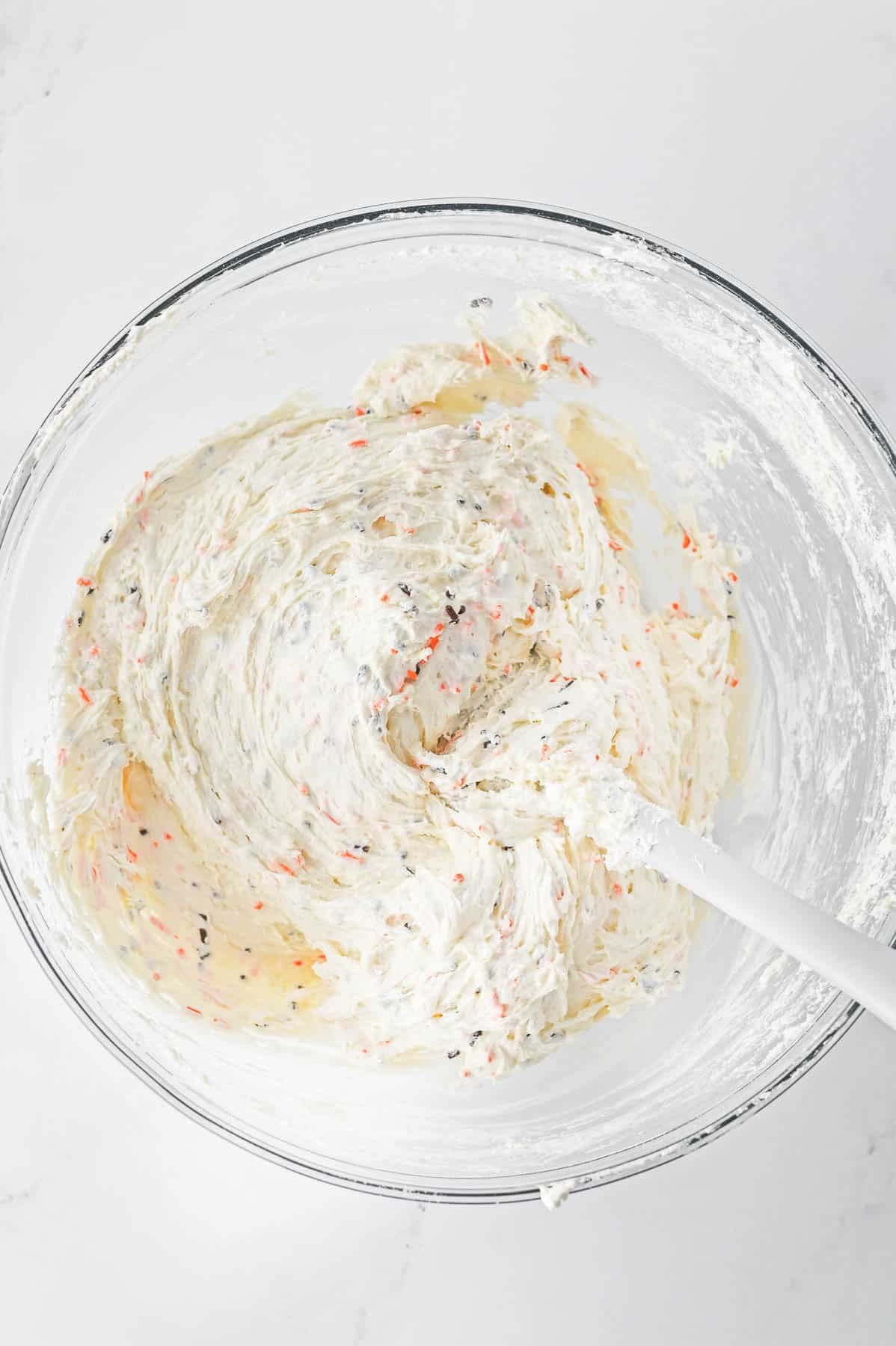 A glass mixing bowl of funfetti dip with sprinkles in it.