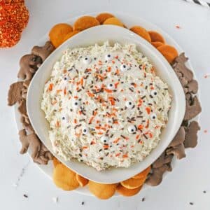 A bowl of funfetti dip topped with orange and chocolate sprinkles and surrounded by chocolate animal crackers and vanilla wafers.
