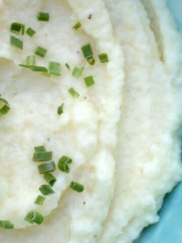 A bowl of mashed cauliflower with chives on top.