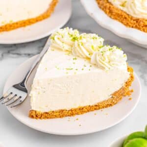 A white plate with a slice of lime pie topped with whipped cream and lime zest.