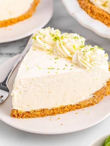 A white plate with a slice of lime pie topped with whipped cream and lime zest.