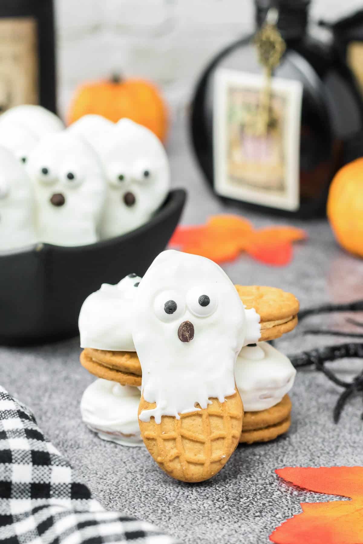Ghost cookie sitting on a table with fall leaves in the background.