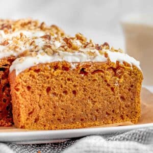 A slice of pumpkin bread with cream cheese frosting and chopped nuts on a plate.