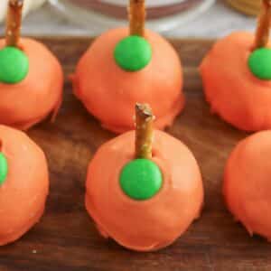 A group of orange pumpkins with green pretzels on a wooden cutting board.