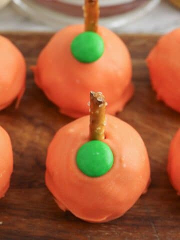 A group of orange pumpkins with green pretzels on a wooden cutting board.