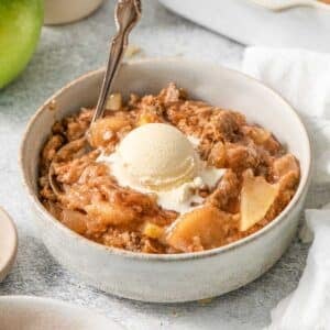 white bowl full of an easy apple dump cake recipe with a scoop of vanilla ice cream and a spoon.