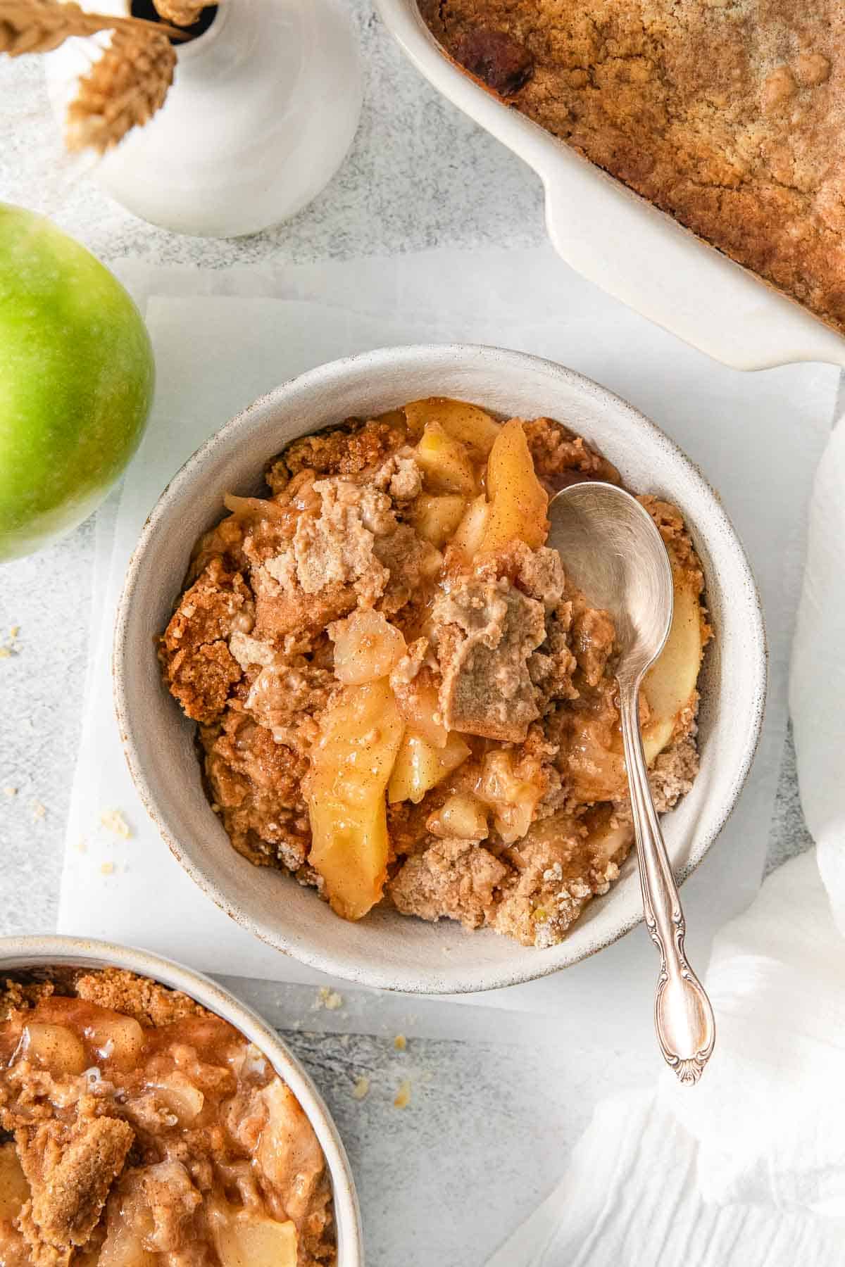 Apple dump cake with crumbly topping in a bowl with a spoon.
