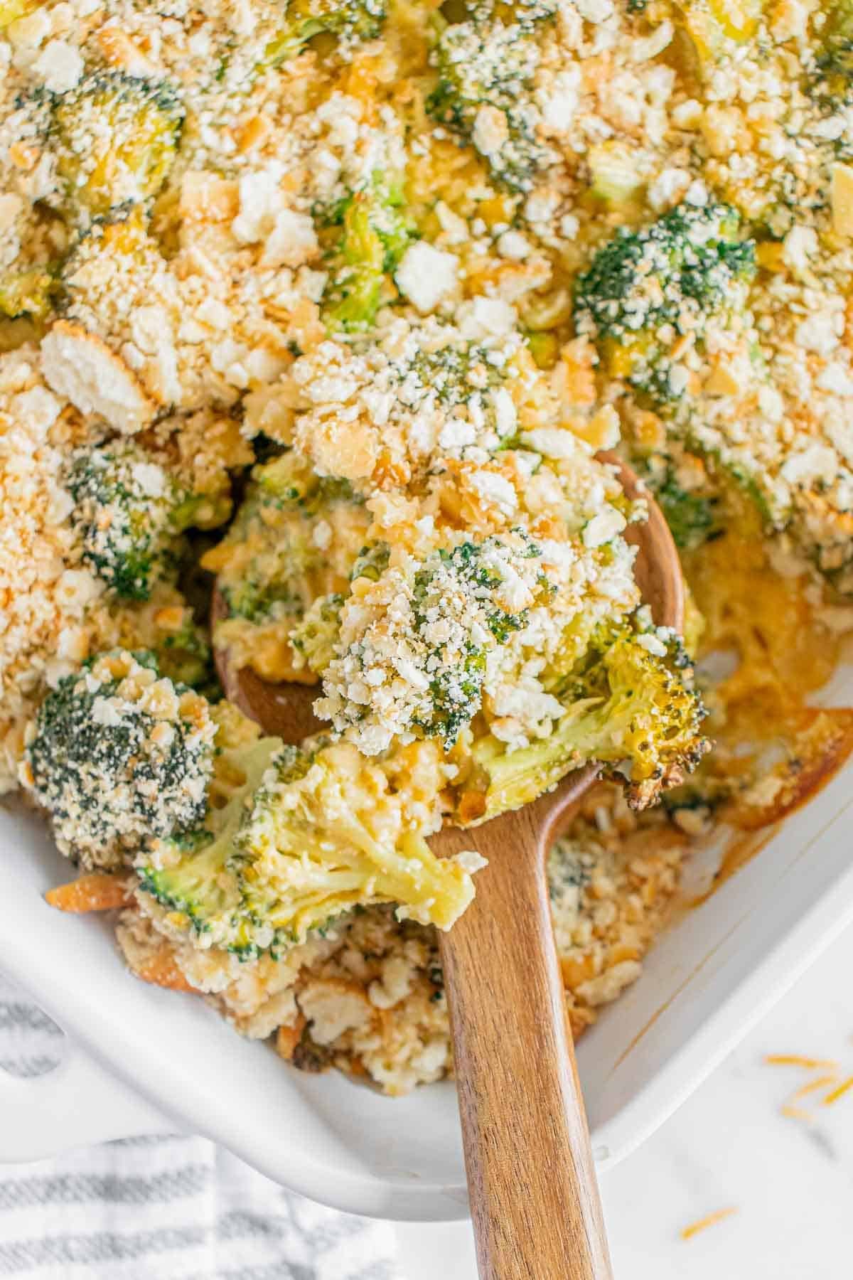 Broccoli casserole in a white dish with a wooden spoon scooping it out.
