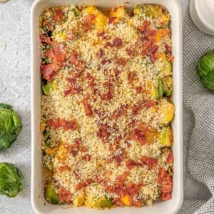 Brussel sprouts casserole in a white baking dish topped with bacon and breadcrumbs.