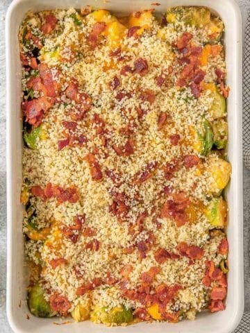 Brussel sprouts casserole in a white baking dish topped with bacon and breadcrumbs.