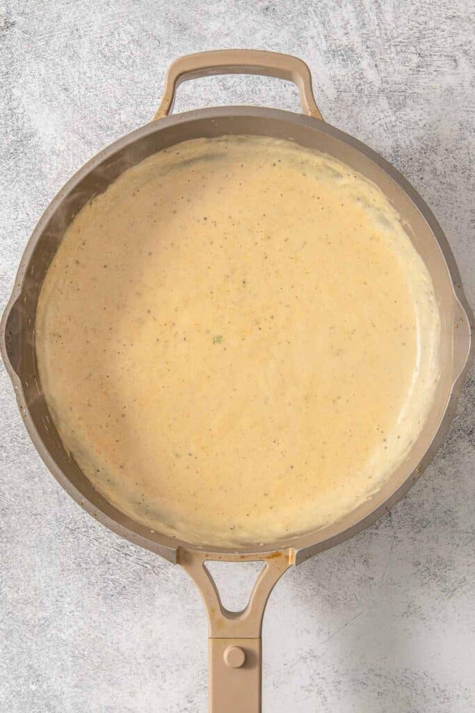 A Brussel Sprout Casserole simmering in a frying pan with a yellow sauce.