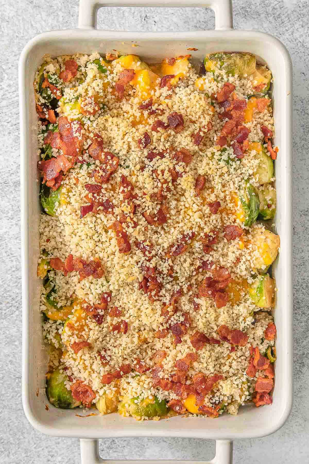 Brussel sprouts casserole in a white baking dish topped with bacon and breadcrumbs.