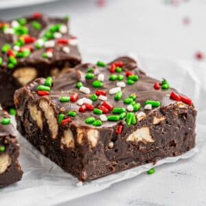 A piece of chocolate fudge with pecans and sprinkles on top.