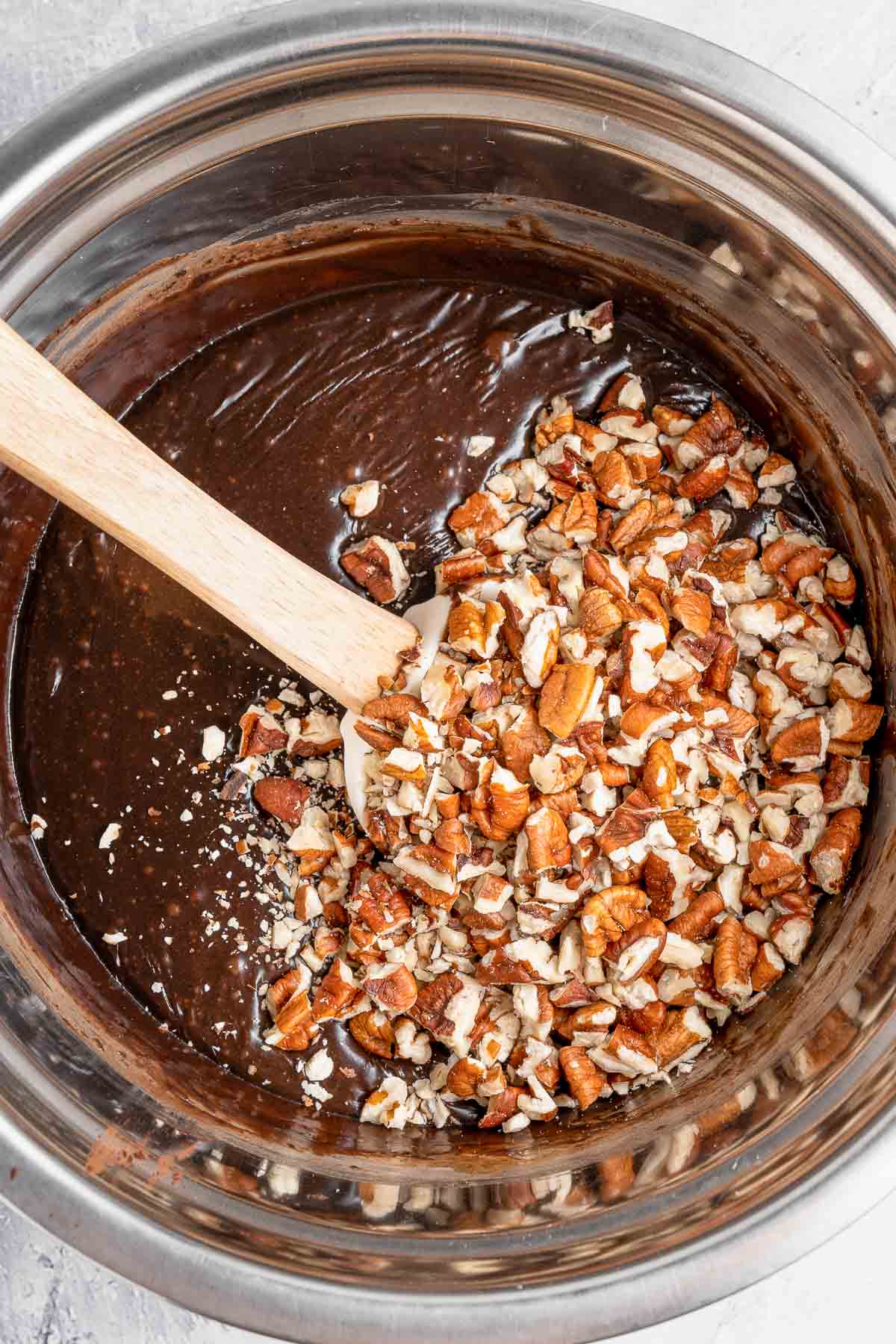 A bowl of melted chocolate with chopped nuts added in and being stirred with a wooden spoon.
