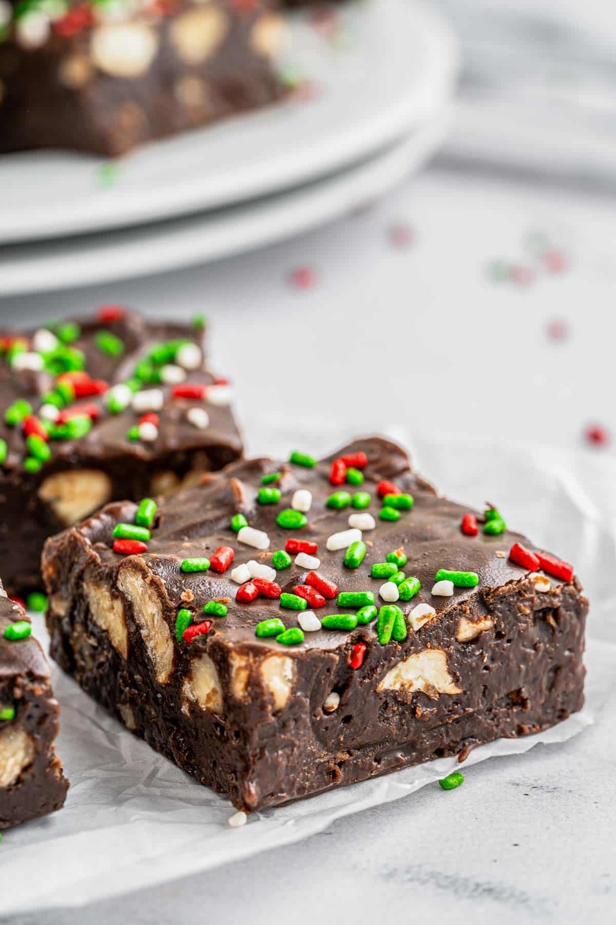 A piece of chocolate fudge with nuts inside and red and green sprinkles on top.